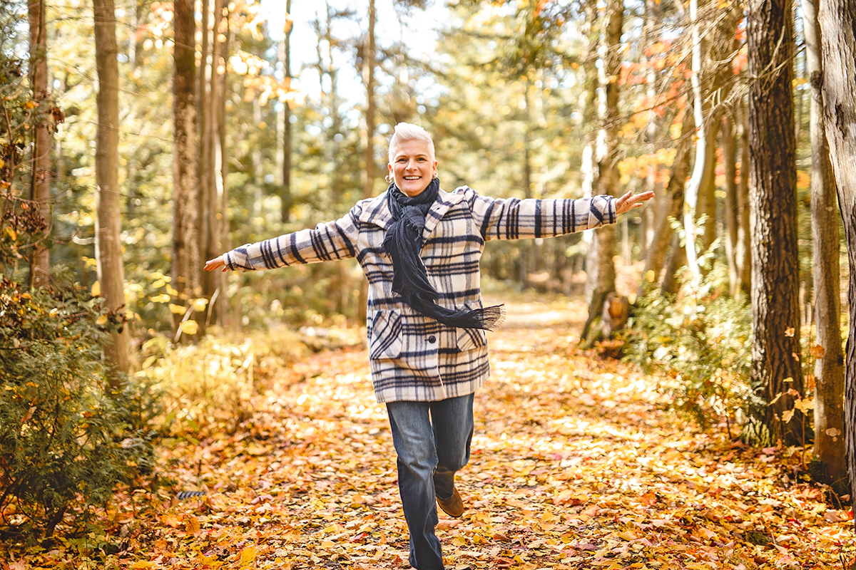 A woman walking joyfully through a Northern Michigan forest in autumn, surrounded by golden fallen leaves